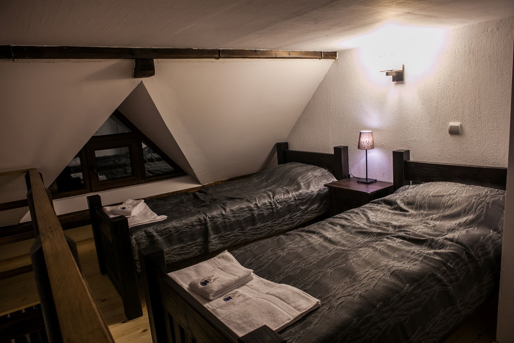 Ein kleiner, schmal beleuchteter Raum mit zwei Einzelbetten, einer Holzleiter und einer geneigten Decke.