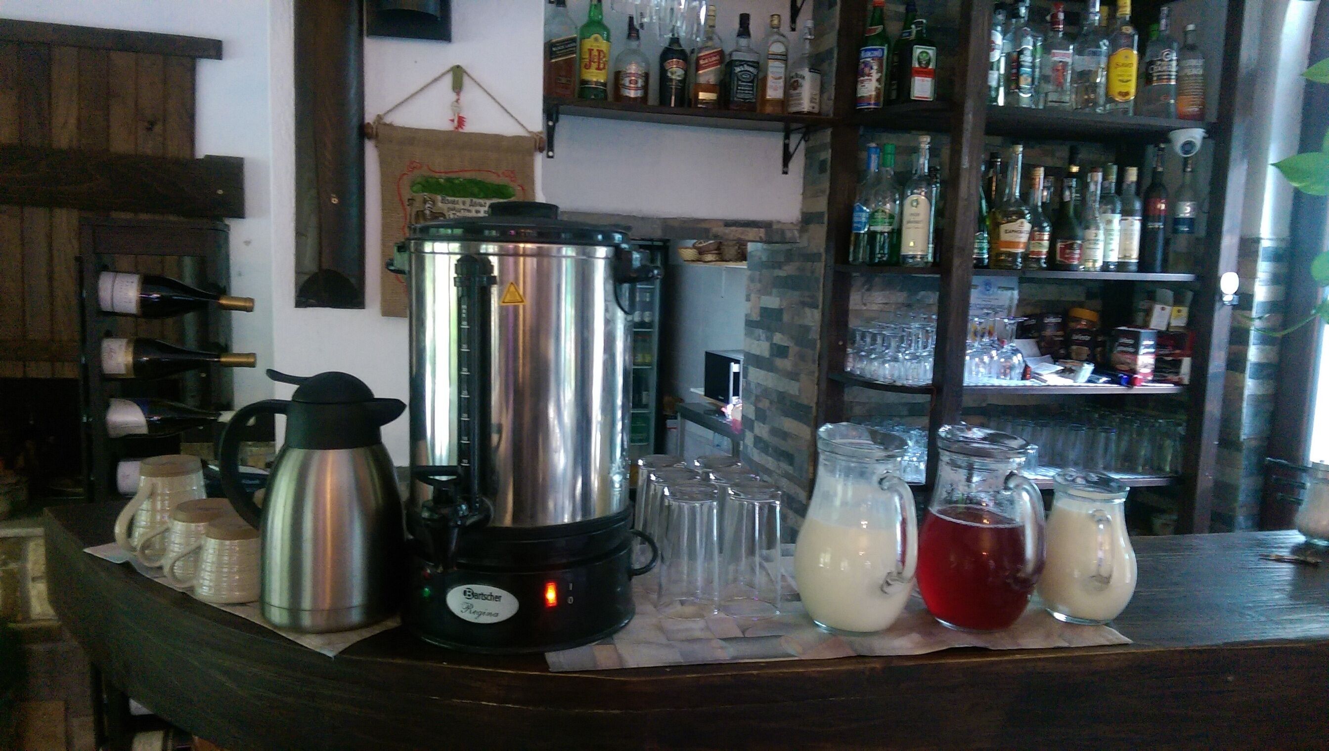 A bar area with a coffee maker, a blender, and various bottles and glasses on shelves.