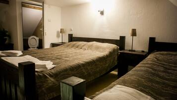 A bedroom with two beds, a bedside table, a lamp, a mirror, and a door.