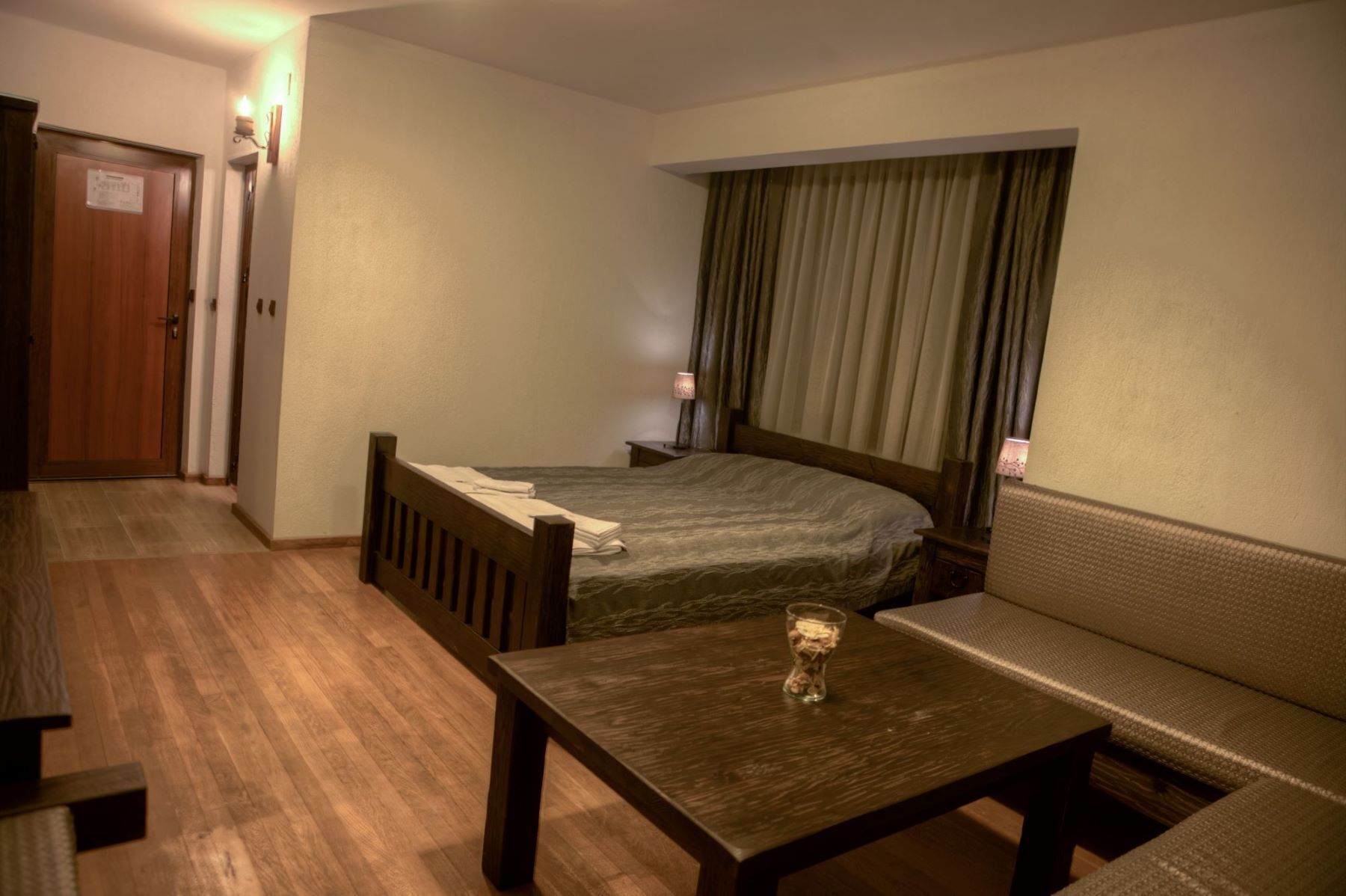 A small, cozy room with a single bed, a bench, a table, and a door.