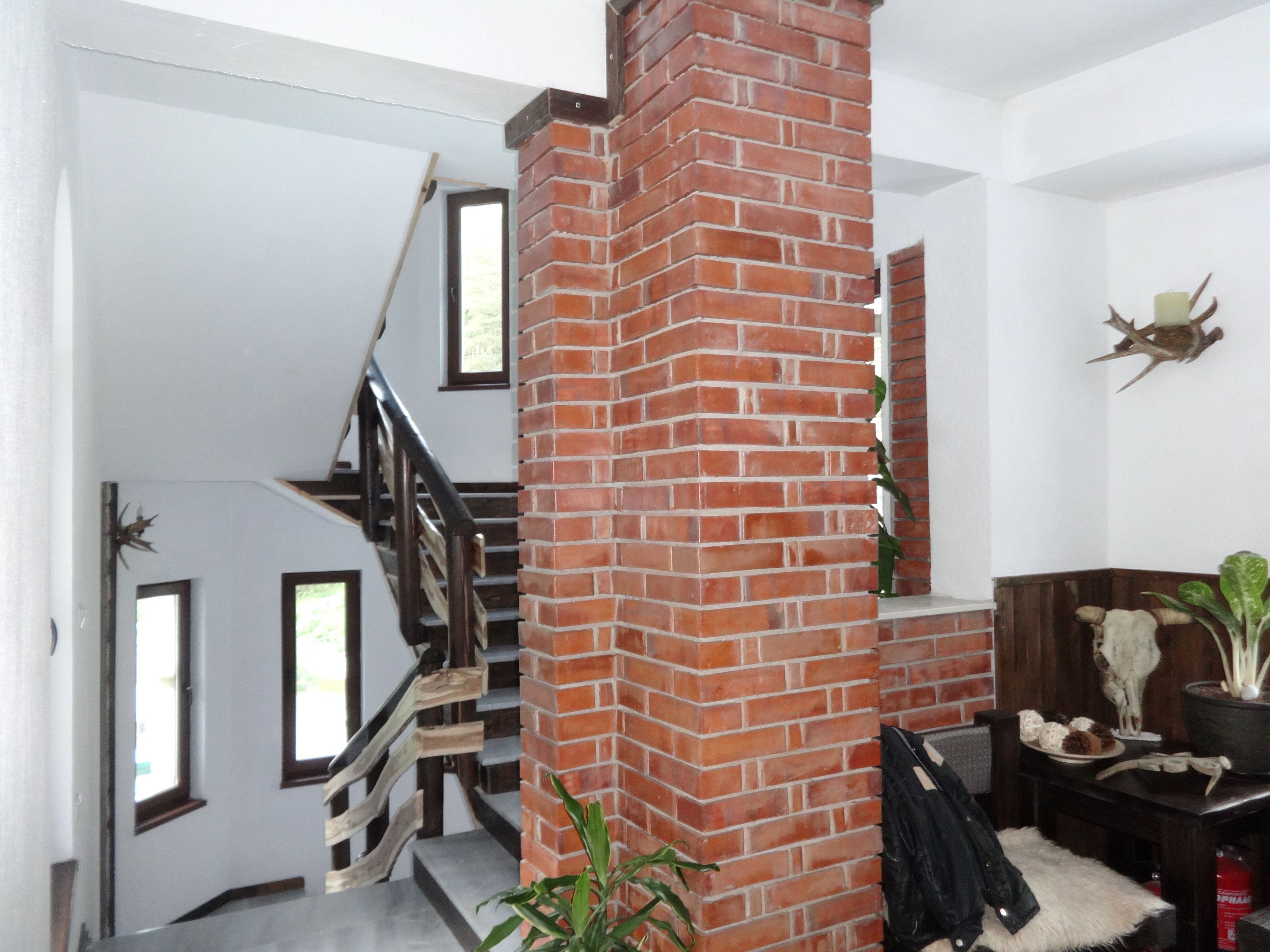 A staircase with a brick column, wooden railings, and a white wall with a mounted deer head.