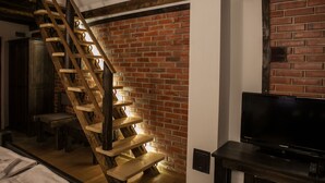 A staircase with wooden steps against a brick wall, a television on a wooden stand, and a bench. - Holiday village Horlog Castle (Devin)