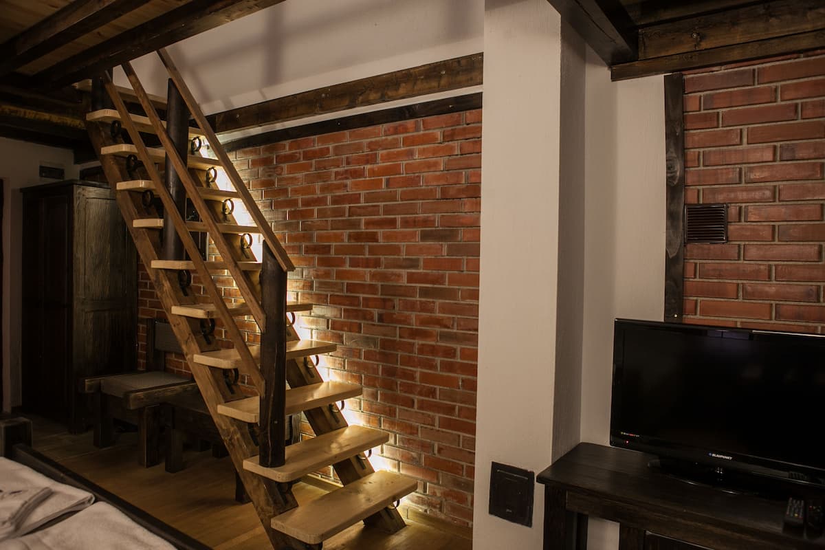 A staircase with wooden steps against a brick wall, a television on a wooden stand, and a bench.