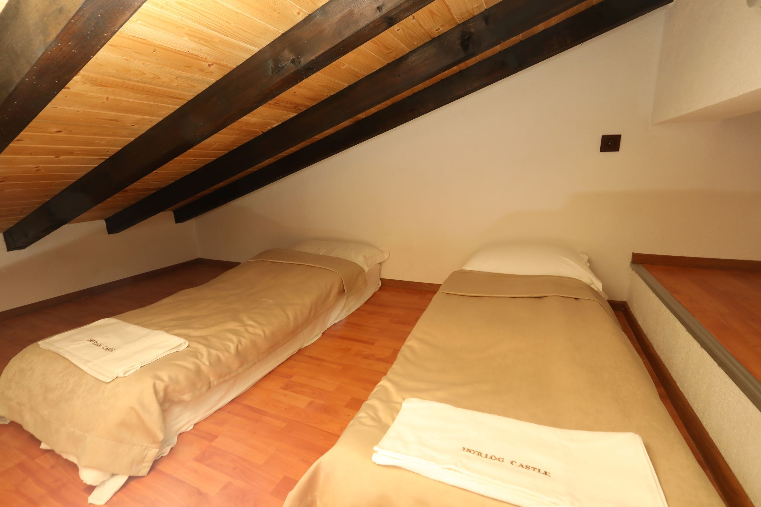 Una habitación pequeña y acogedora con dos camas individuales, vigas de madera en el techo y suelo de madera.