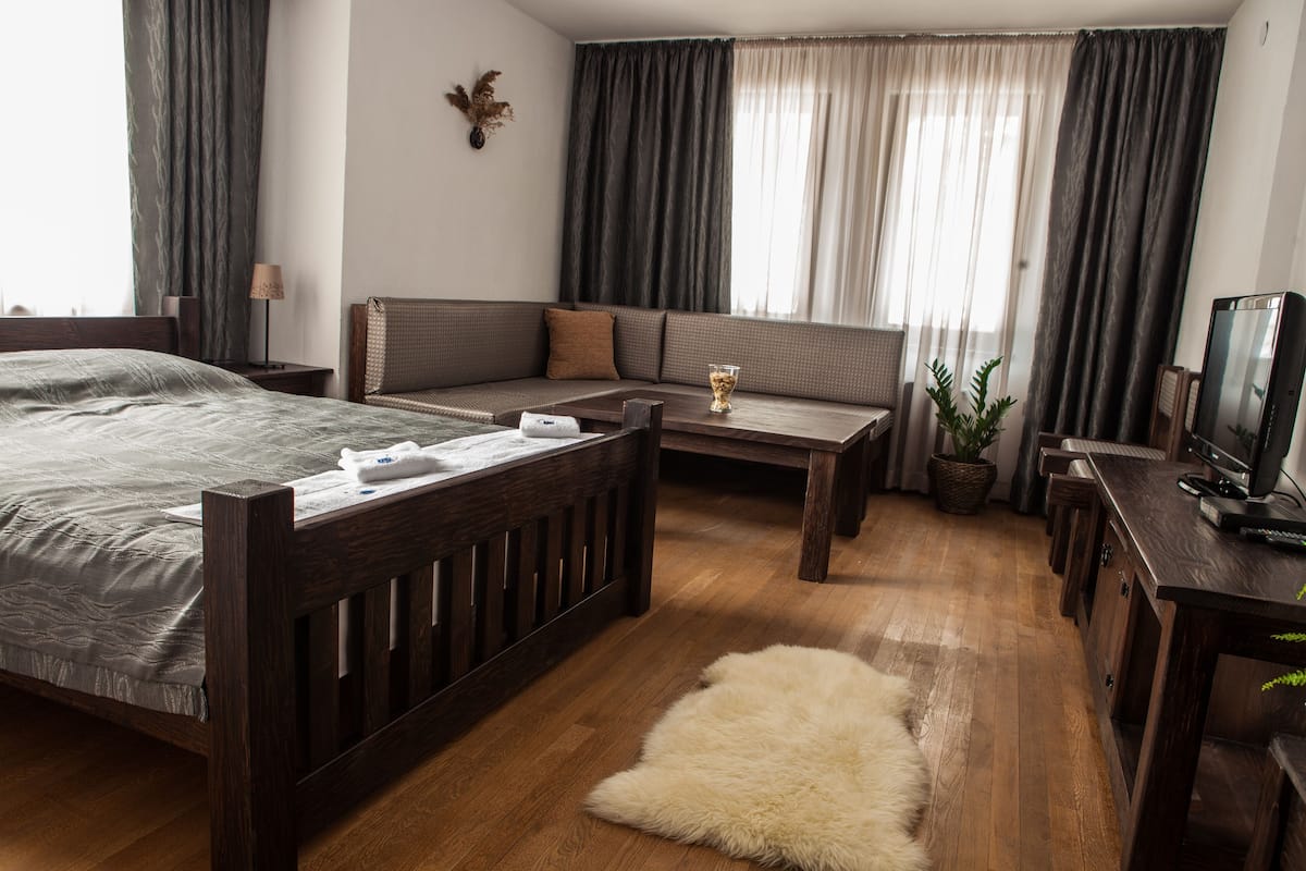 A hotel room with a bed, a sofa, a small table, a TV, and a potted plant.