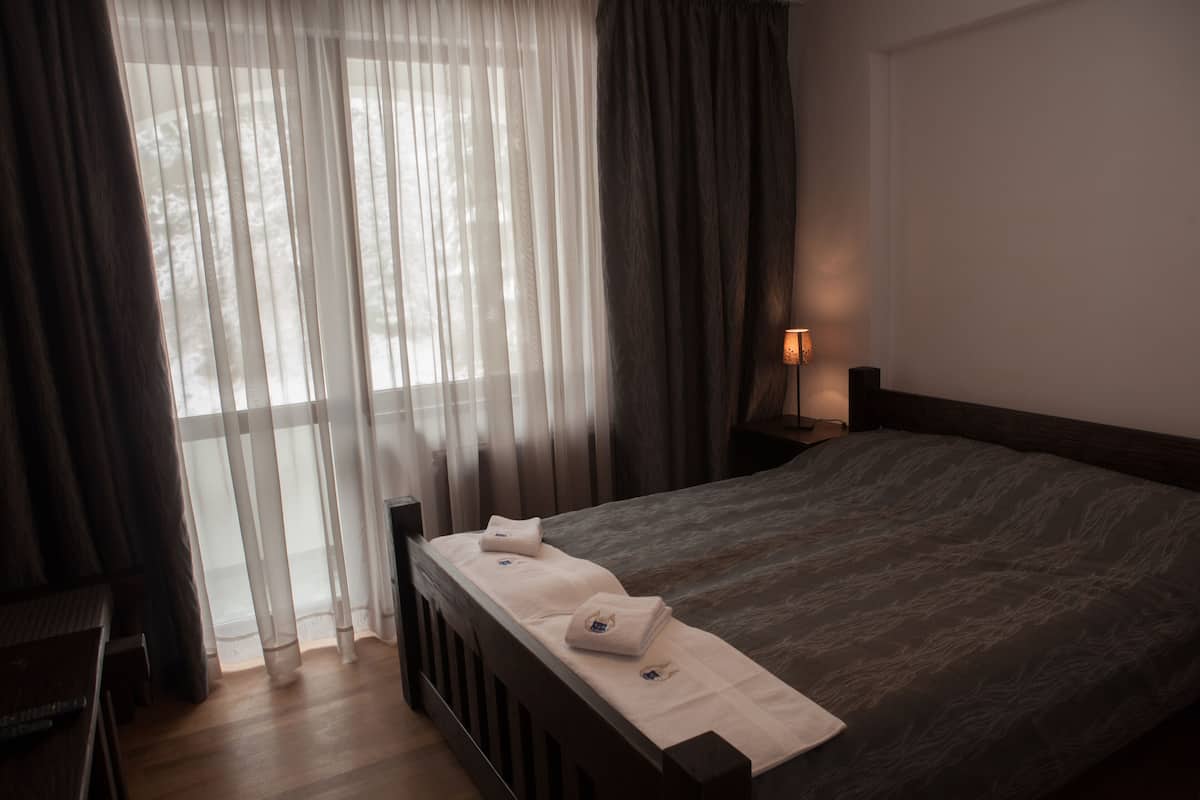 A bedroom with a large bed, a bedside table, a lamp, and sheer curtains.