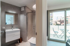 A modern bathroom with a glass shower enclosure, a white vanity with a mirror, and a view of the outside balcony through a sliding glass door. - Kristall 9  (Massagno)
