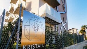 A chain-link fence with a sign that reads "KRISTALL" and a geometric logo. - Kristall 9  (Massagno)