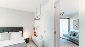 A modern bedroom with a bed, bedside table, and a nightstand. There is a sofa and a small table in the adjacent living area. - Kristall 9  (Massagno)