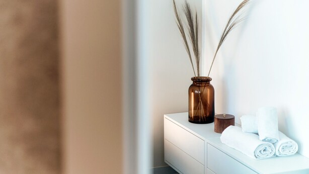 A bathroom with a white vanity, a brown vase with pampas grass, and rolled towels. - Kristall 9  (Massagno)