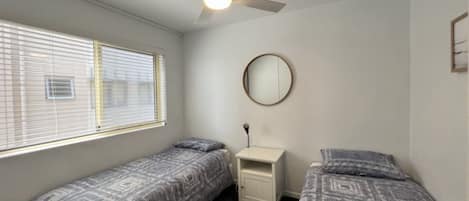 A bedroom with two single beds, a ceiling fan, a bedside table, and a round mirror.