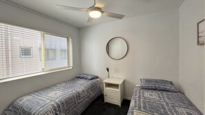A bedroom with two single beds, a ceiling fan, a bedside table, and a round mirror. - Dulkara 7 3Br Unit Steps From Kings Beach (KINGS BEACH)