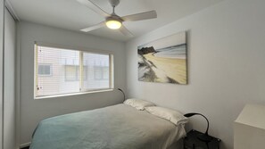 A bedroom with a bed, a ceiling fan, a window with blinds, and a painting on the wall.
