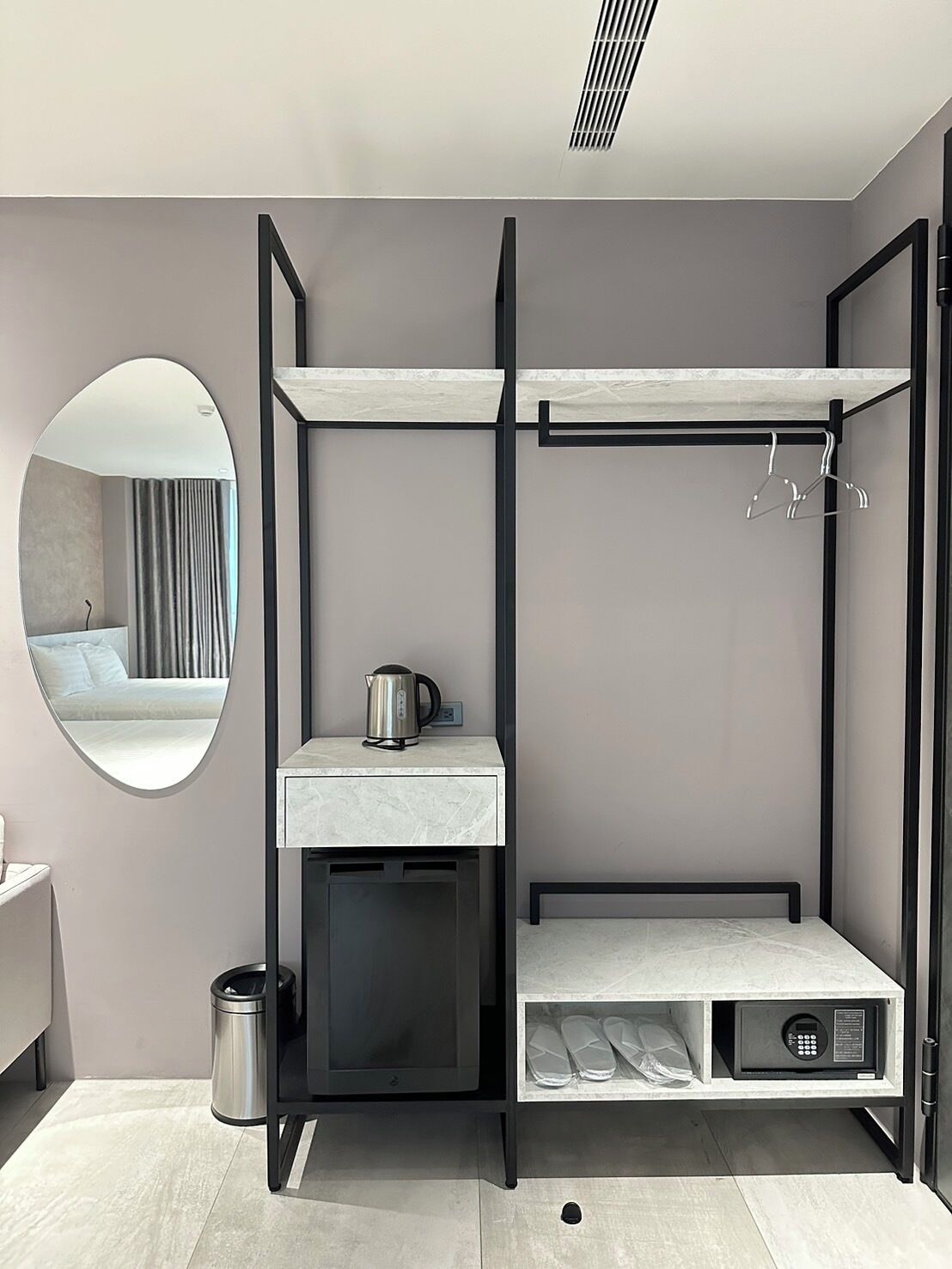 Una habitación moderna y compacta con una cama litera, un pequeño espacio kitchenette, un espejo y un cesto de basura.