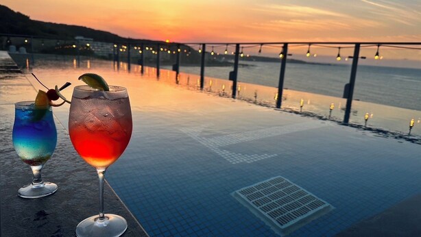 Zwei Cocktails am Pool im Freien mit Blick auf einen Sonnenuntergang.