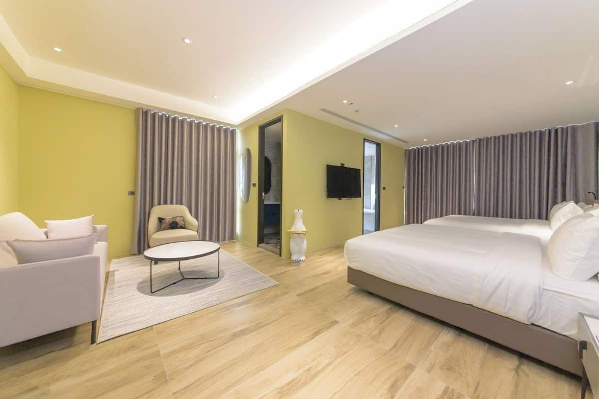 Ein modernes Hotelzimmer mit einem großen Bett, einem Sofa, einem runden Couchtisch und einem an der Wand befestigten Fernseher.