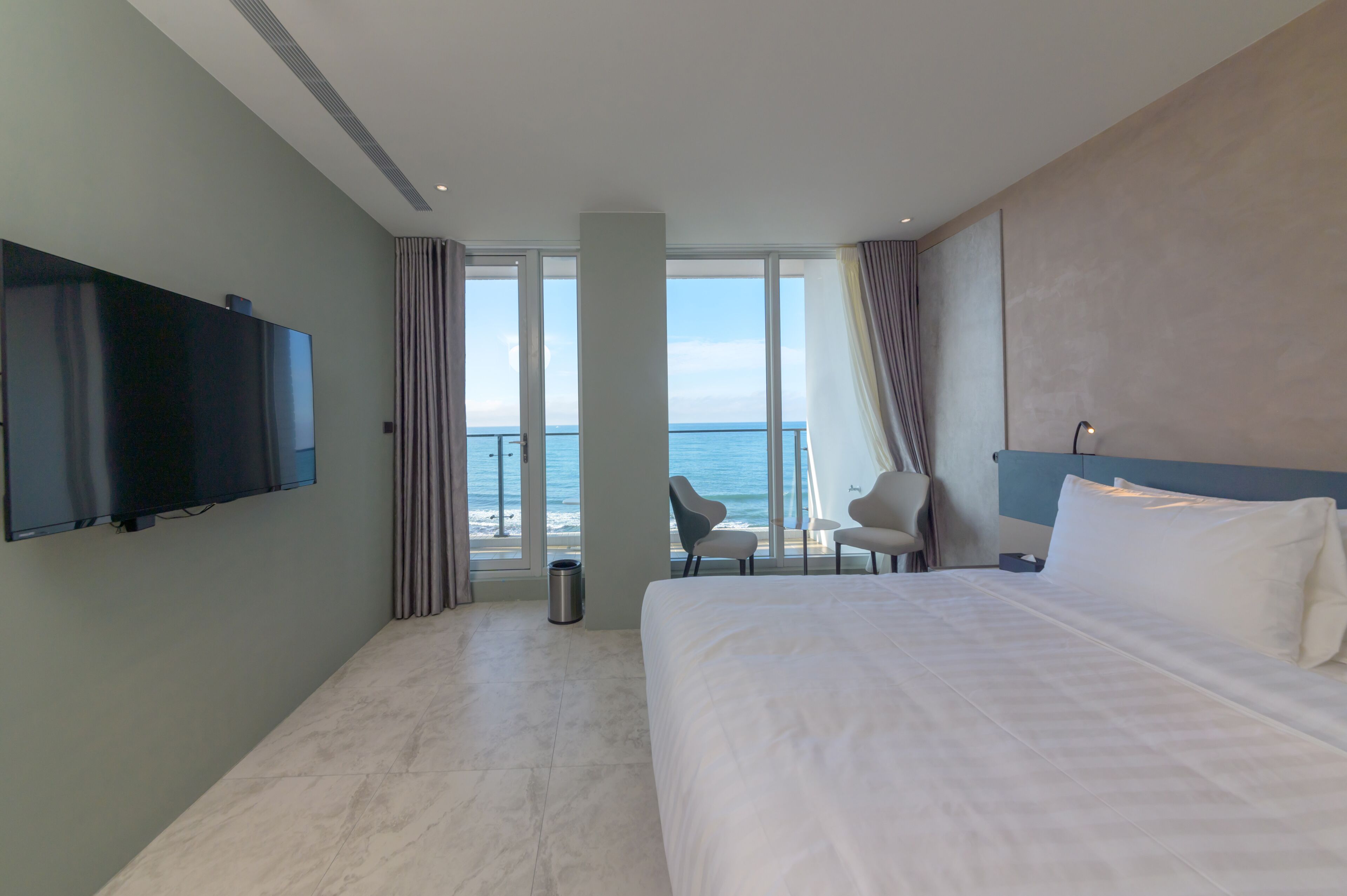 Camera d'albergo con un letto grande, una TV a schermo piatto, un’area salotto con poltrone e vista sull'oceano.