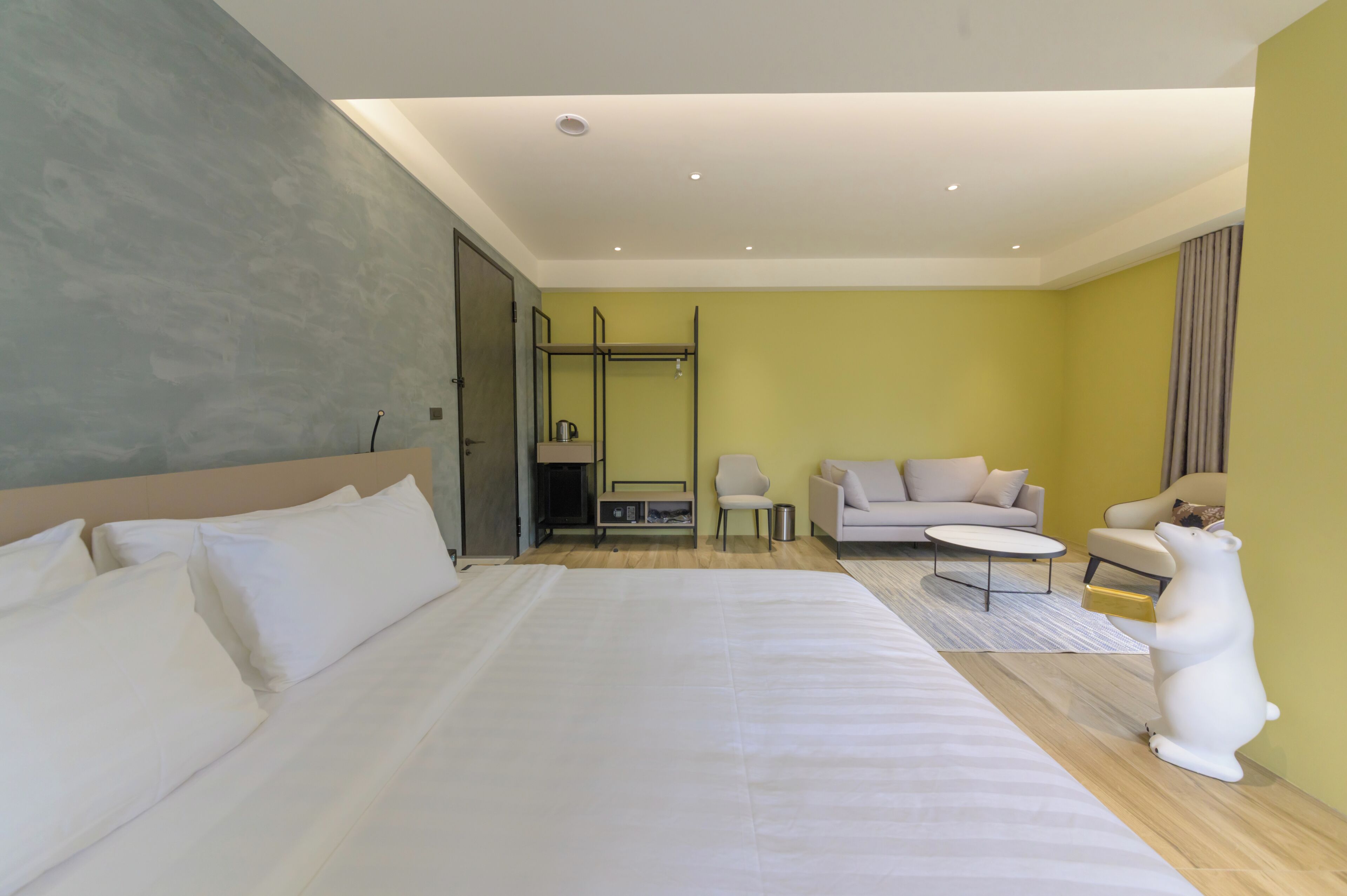 Una habitación de hotel moderna con una cama grande, un sofá, una mesa de centro y una estatua de un oso polar.