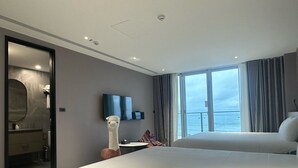 Ein modernes Hotelzimmer mit einem großen Bett, einem Fernseher, einem Spiegel und Meerblick.
