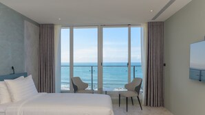 Ein Hotelzimmer mit einem großen Bett, zwei Sesseln, einem Fernseher und einem Balkon mit Meerblick.