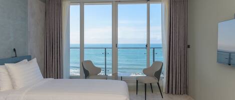 Ein Hotelzimmer mit einem großen Bett, zwei Sesseln, einem Fernseher und einem Balkon mit Meerblick.