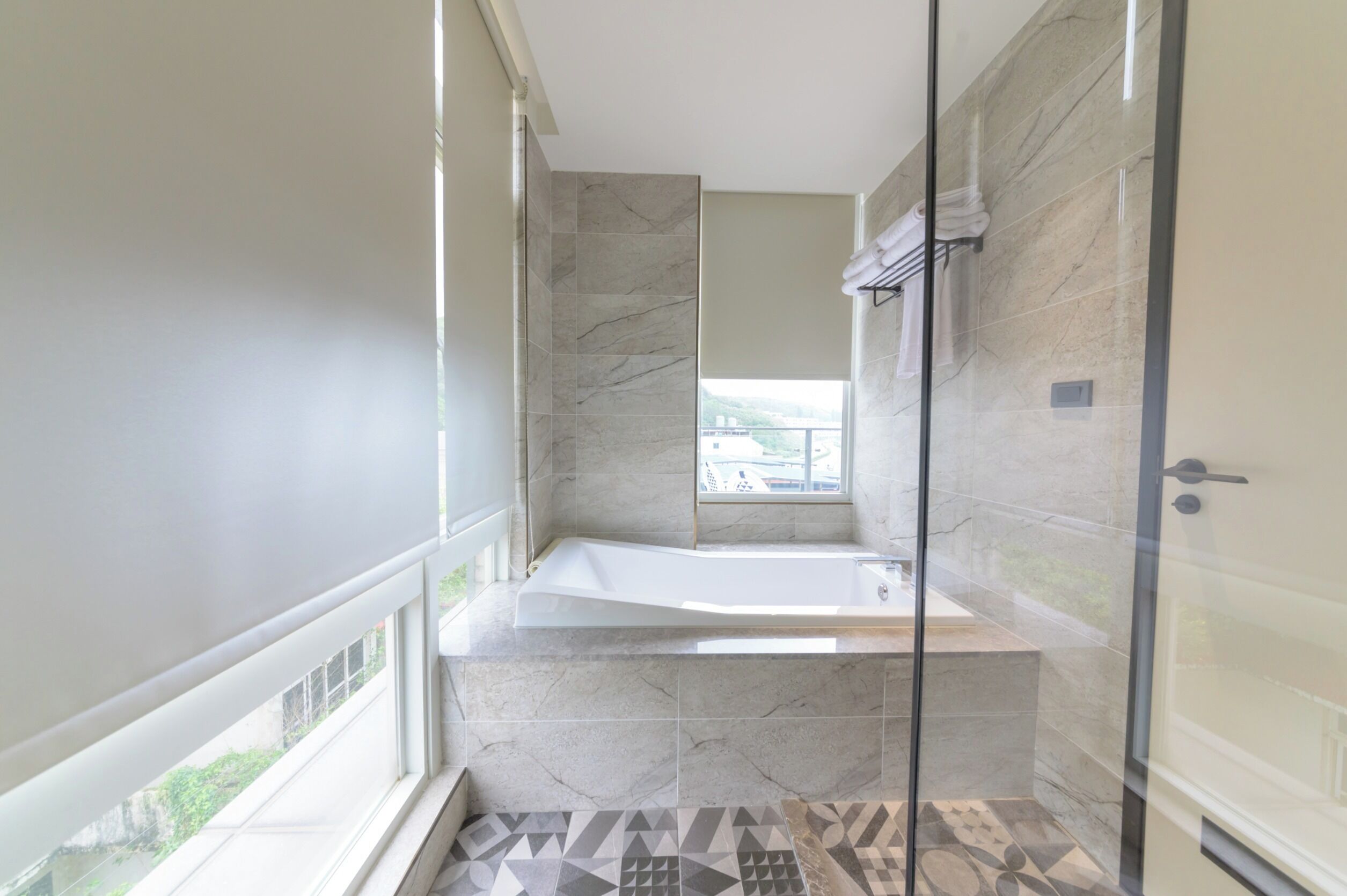 A modern bathroom with a glass-enclosed shower, a freestanding bathtub, and a large window providing a view of the outdoors.