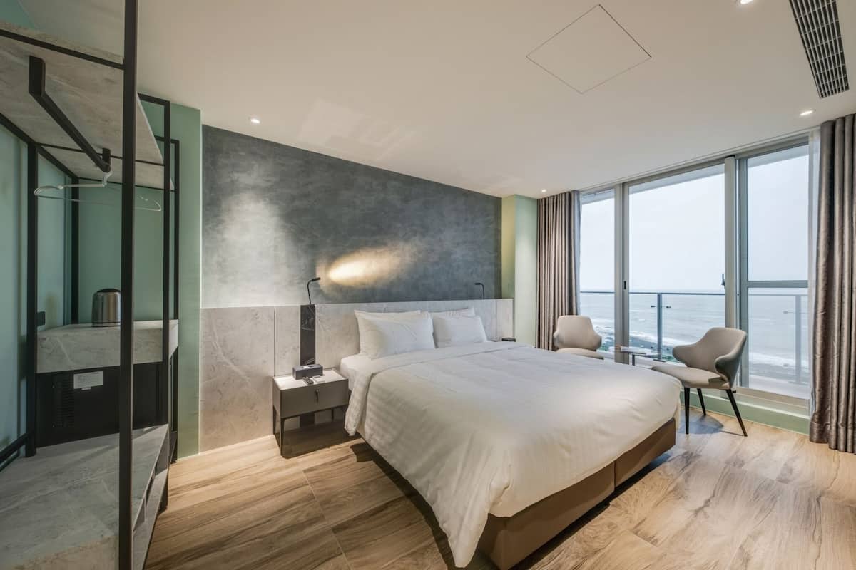 Ein modernes Hotelzimmer mit einem großen Bett, einem Nachttisch, einem Spiegel und Meerblick.