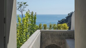 A view through an arched doorway overlooking a coastal landscape with a clear sky and a rocky shoreline.