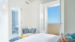 A bedroom with a bed, a chair, and a balcony with a view.