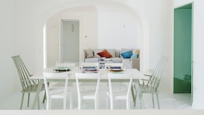 A dining area with a white table and chairs, a sofa with cushions, and a green door in the background.