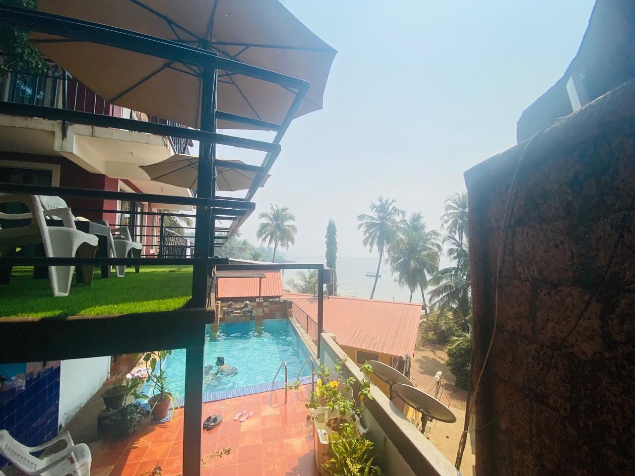 A pool area with a view of the sea, a covered seating area, and a building with balconies.