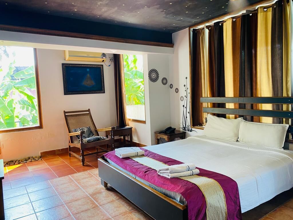 A hotel room with a large bed, a desk, a chair, and a view of greenery outside.