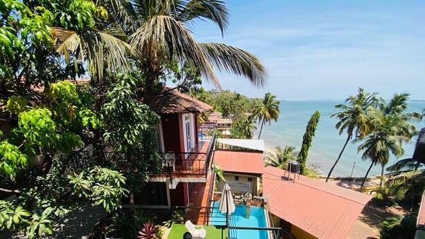 Un edificio su due piani con piscina, immerso nel verde rigoglioso e palme, con vista su una spiaggia.