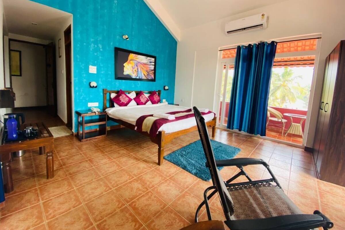 Ein Schlafzimmer mit Bett, Stuhl, Schreibtisch, einem Bild und Blick ins Freie.