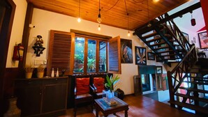 Un accogliente soggiorno con soffitto in legno, una scala e vista sul verde attraverso ampie finestre.