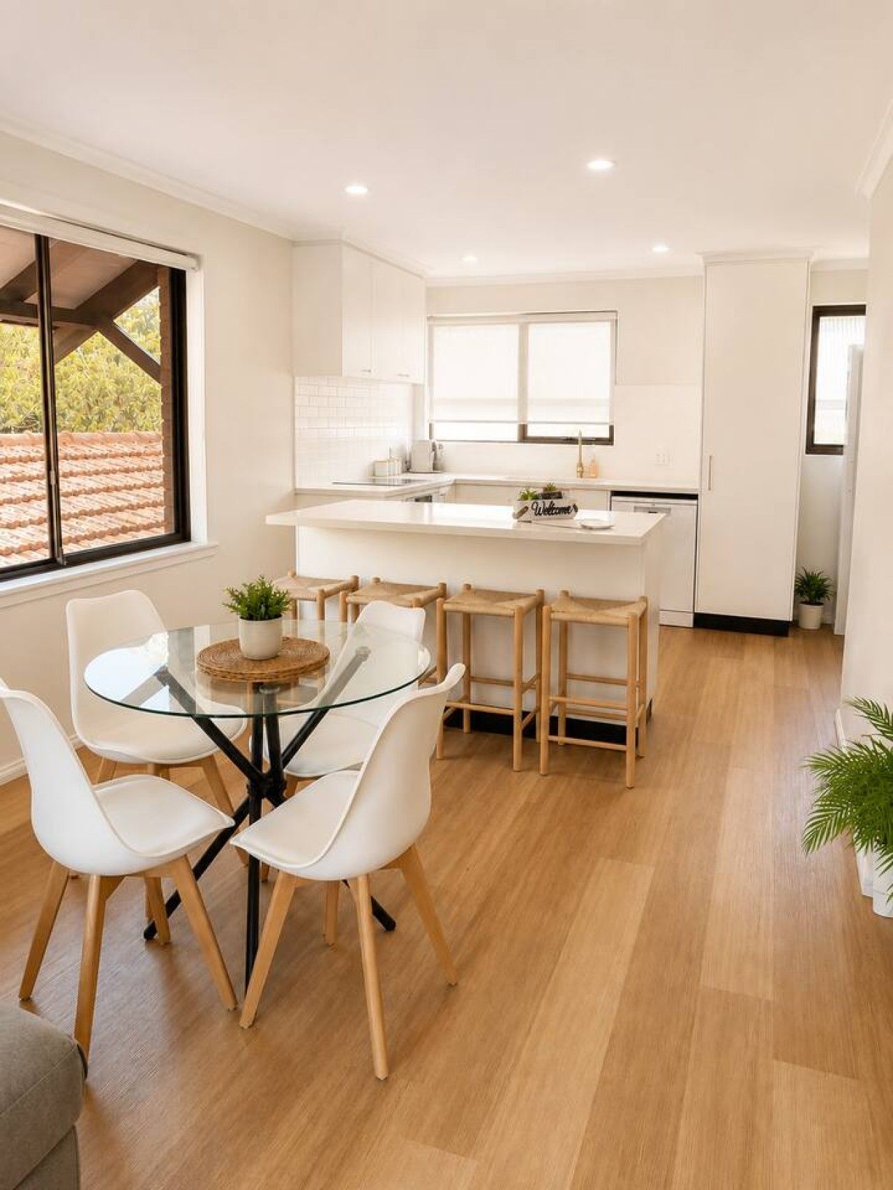 A modern kitchen with a central island, white cabinetry, and a dining area with a glass table and white chairs.