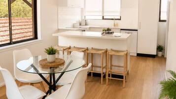 A modern kitchen with a central island, white cabinetry, and a dining area with a glass table and white chairs.