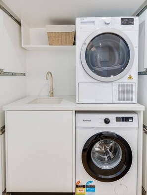A compact laundry area with a washing machine and dryer, a sink, and a shelf above the dryer.