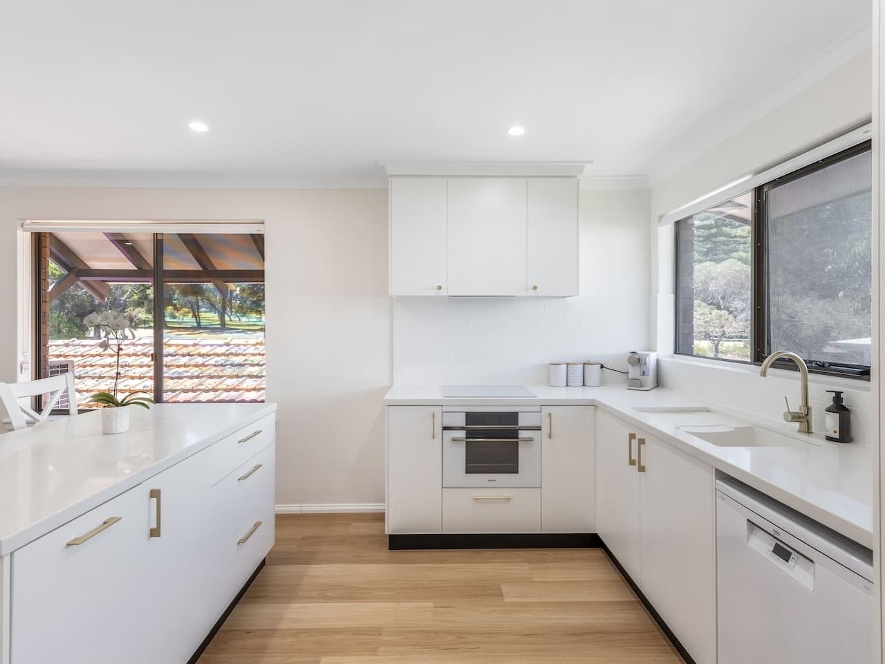 A modern kitchen with white cabinetry, a built-in oven, and a window providing a view of the outdoors.