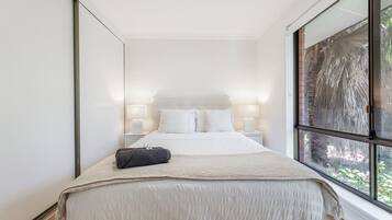 A bedroom with a large bed, bedside lamps, and a view through a window.