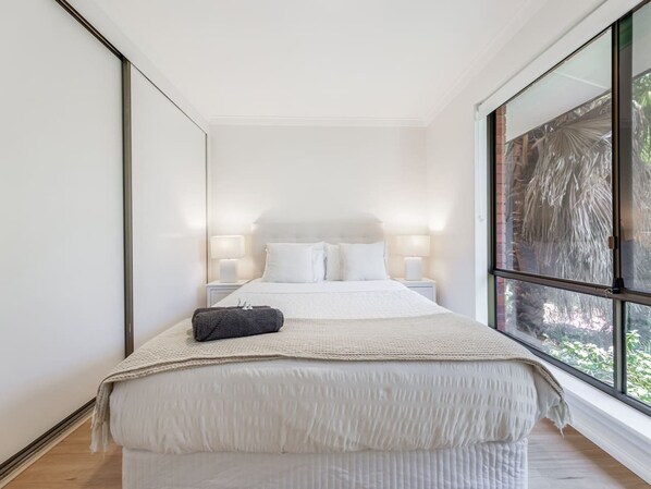 A bedroom with a large bed, bedside lamps, and a view through a window.