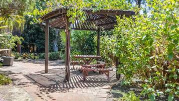 A wooden pergola with a bench and picnic table in a garden setting.