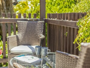 A wicker outdoor seating area with a glass table, two chairs, and a small potted plant.