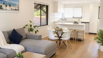 A modern living room with a grey sofa, a coffee table, and a dining area with a small table and chairs.