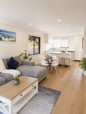 A modern living room with a grey sofa, a coffee table, and a dining area with a small table and chairs.