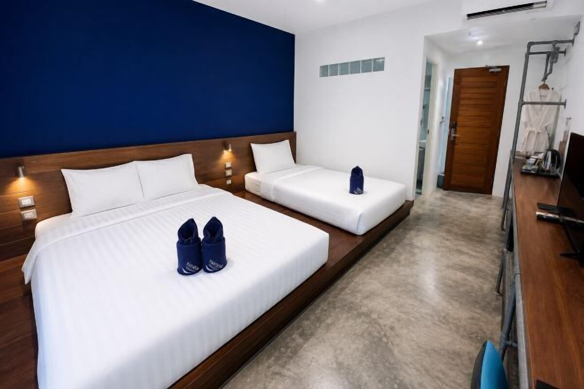 Een hotelkamer met twee bedden, een houten hoofdeinde, een blauwe accentmuur, een kleine badkamer met douche en een houten vloer.