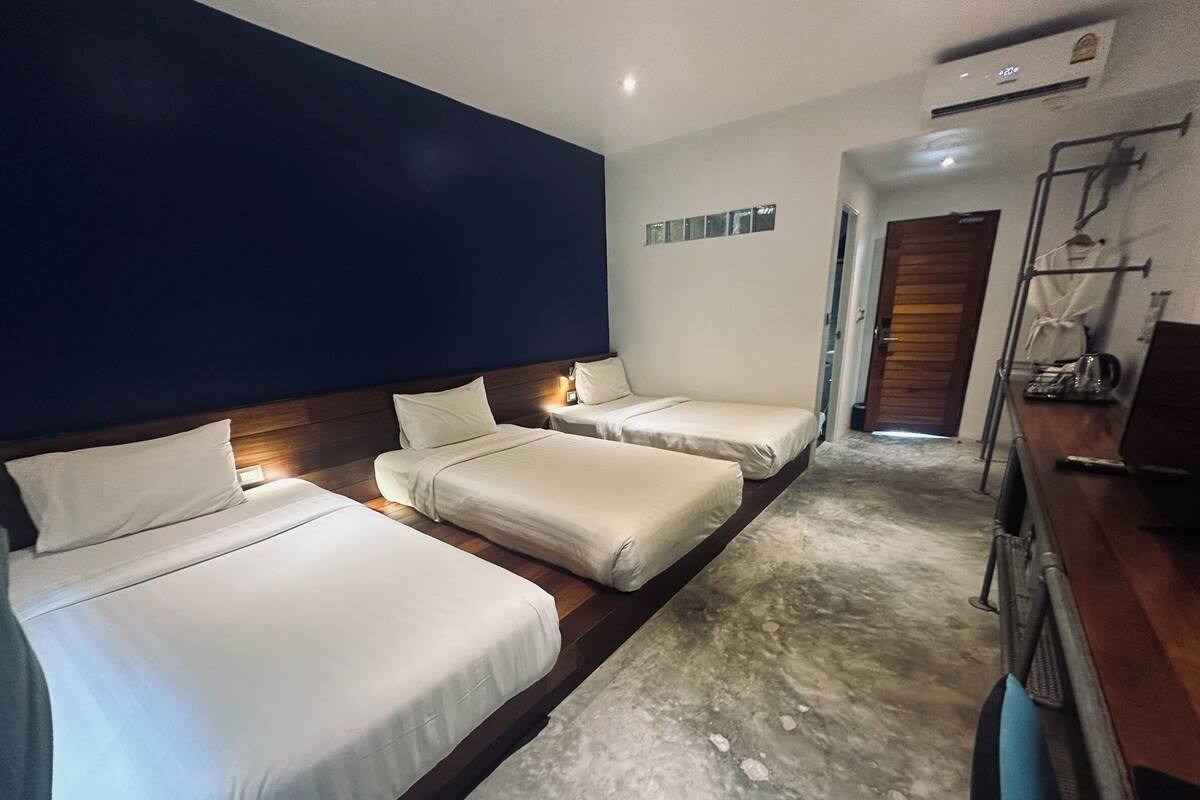 Une chambre d’hôtel avec deux lits simples, une tête de lit en bois, un petit bureau avec une chaise et une kitchenette.