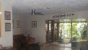 Ein Wohnzimmer mit Deckenventilator, einer Couch, einem Couchtisch und einer Glastür, die auf einen Balkon führt.