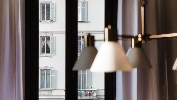 A view through a window with a curtain, revealing a building with multiple windows and a balcony. - STELLA APARTMENT  (Como)