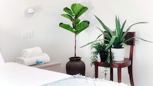 A neatly made bed with rolled white towels, a vase with a single plant, and a chair with multiple potted plants. - STELLA APARTMENT  (Como)